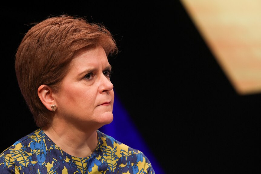 A close up of Nicola Sturgeon frowning as she looks away from camera in a blue and yellow outfit.