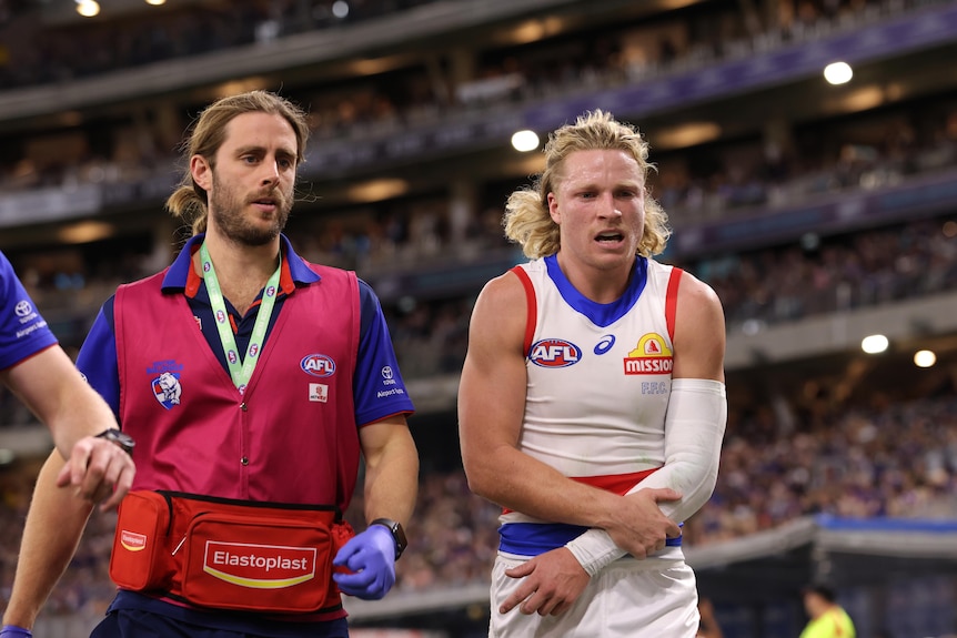 A Western Bulldogs player grimaces as he walks off the ground holding his arm.