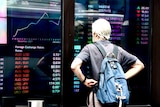A man with a backpack looks at a screen with currency prices in the red at the Australian Security Exchange (ASX)