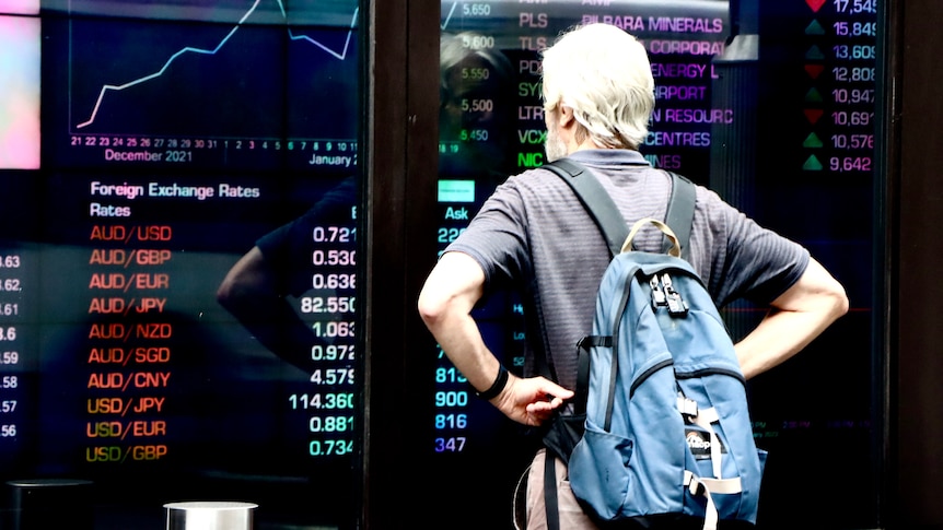 A man with a backpack looks at a screen with currency prices in the red at the Australian Security Exchange (ASX)