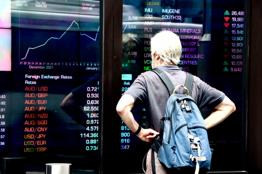 A man with a backpack looks at a screen with currency prices in red at the Australian Security Exchange (ASX)