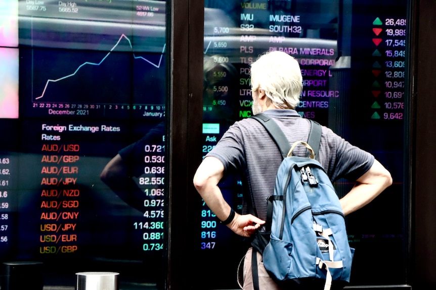 A man with a backpack looks at a screen with currency prices in the red at the Australian Security Exchange (ASX)