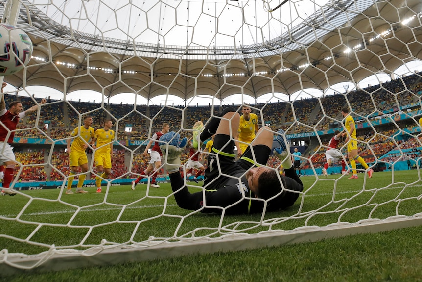 A footballer raises his arms in the air in triumph as the ball nestles in the net and the keeper lies helpless on the ground