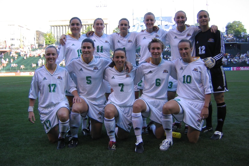 A women's soccer team wearing white and green poses for a photo before a game
