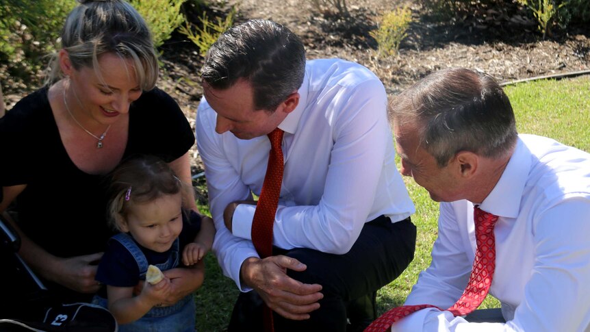 Mark McGowan and Roger Cook speak to a mother and her child crouched on a lawn.