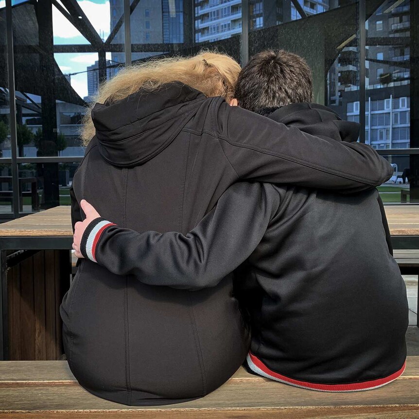 A de-identified image of a mother and son sitting with their arms around each other