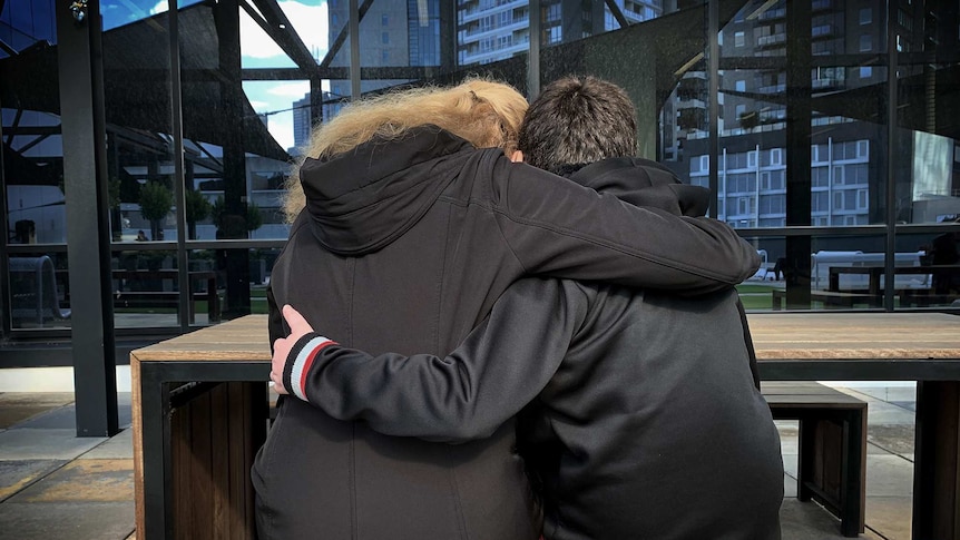 A woman and boy hug as they sit together (as seen from behind).