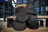 A woman and boy hug as they sit together (as seen from behind).