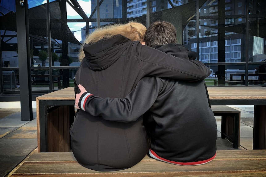 A de-identified image of a mother and son sitting with their arms around each other