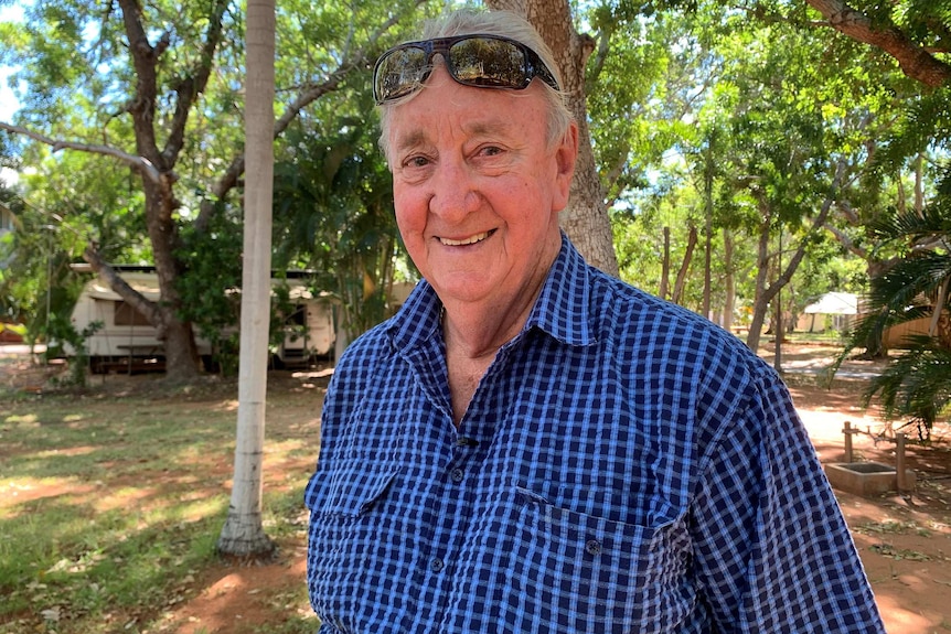 A mid shot of Cable Beach Caravan Park owner Ron Beacham smiling for a photo standing outside in a blue checked shirt.