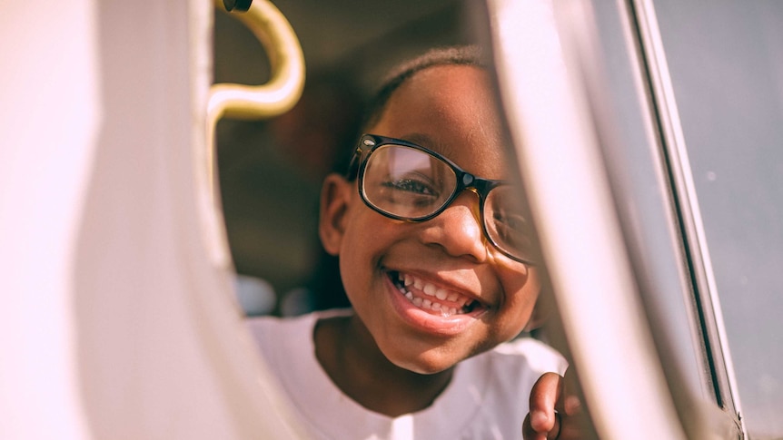 A boy with heavy glasses frames flashes a toothy grin
