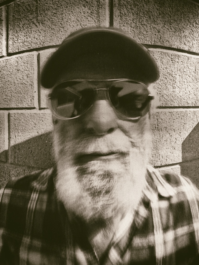 A black and white portrait of a man wearing sunglasses and a hat.