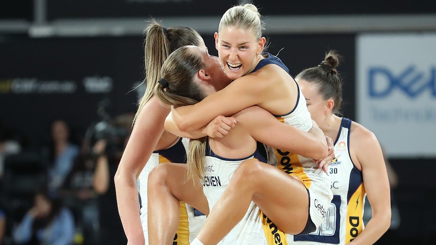 A woman in a netball uniform jumps into the arms of her teammate