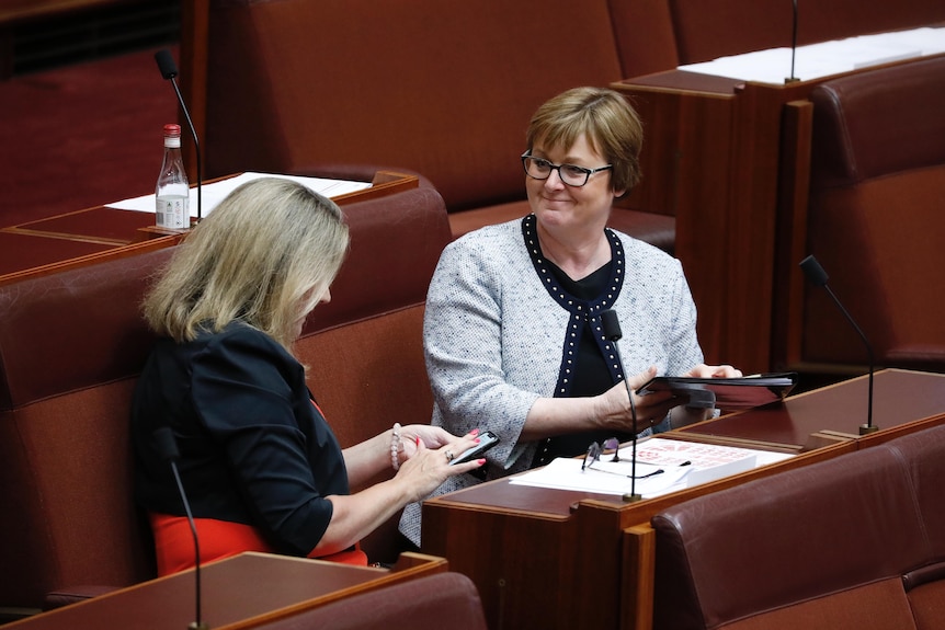 Two women sitting in at a desk on red seats