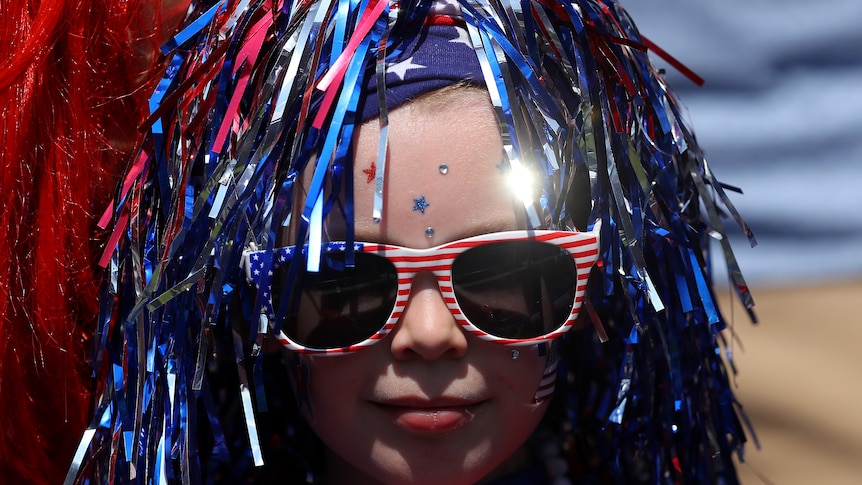 A young girl is wearing a red, white and blue wig with red glasses.