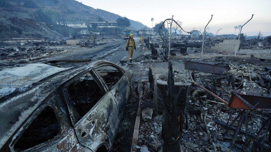 A firefighter walks down a street with nothing more than rubble and a burned out car on the street.