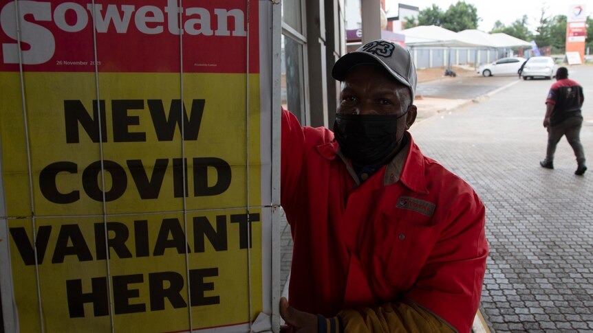 A petrol attendant stands next to a newspaper headline saying "new COVID variant here"  in Pretoria.