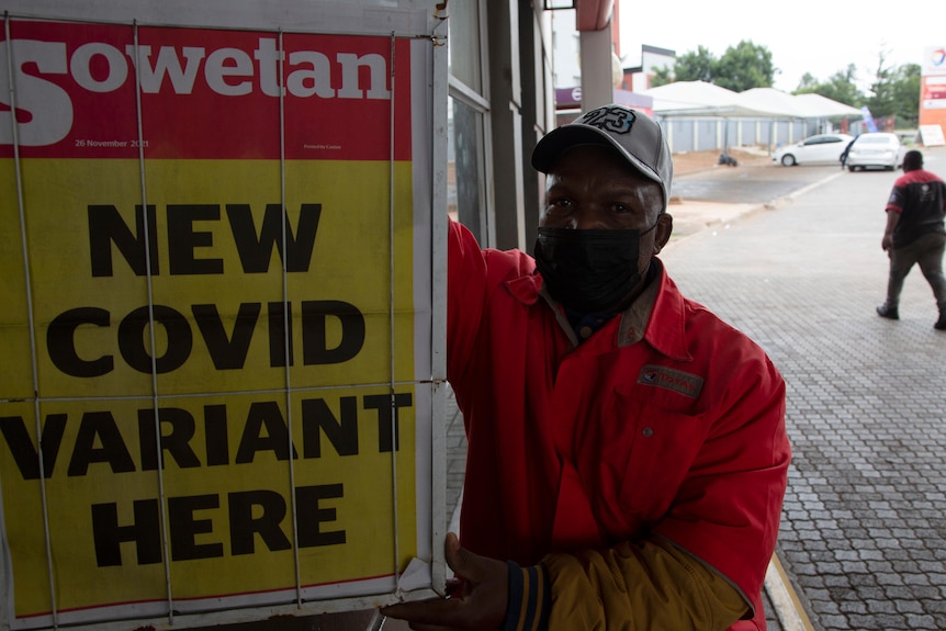 A petrol attendant stands next to a newspaper headline saying "new COVID variant here"  in Pretoria.