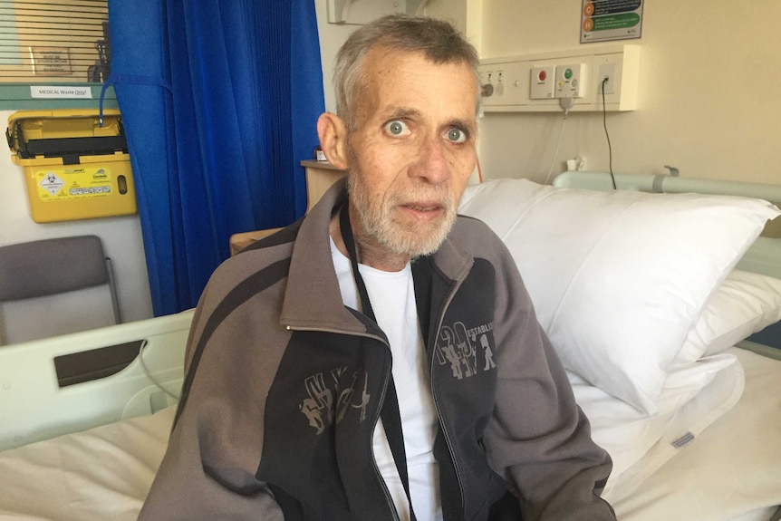 Palliative care patient John Chandler sits on a bed