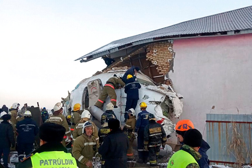 A crowd of rescue workers climb the nose of a jet that has crashed into the side of a pale pink house.