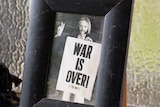 A framed photo of Ritchie Yorke, in 1969, holding a War Is Over poster.