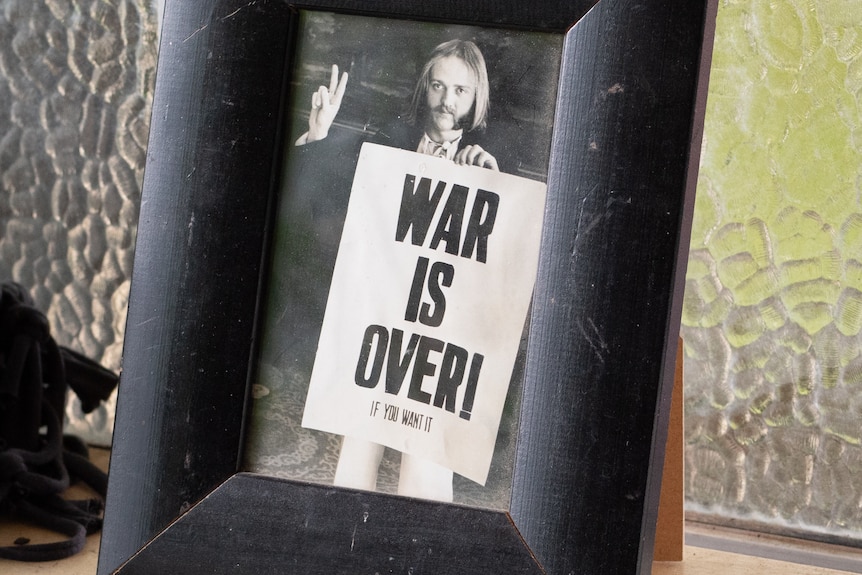 A framed photo of Ritchie Yorke, in 1969, holding a War Is Over poster.