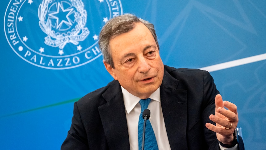 Italian Premier Mario Draghi speaks in front of a blue backdrop.