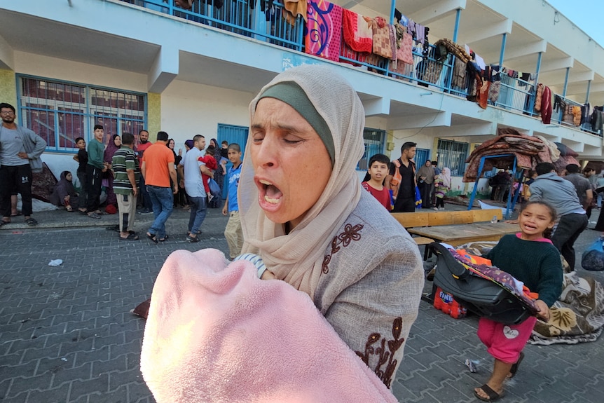 woman carrying a child's body covered with a blanket looks distressed 