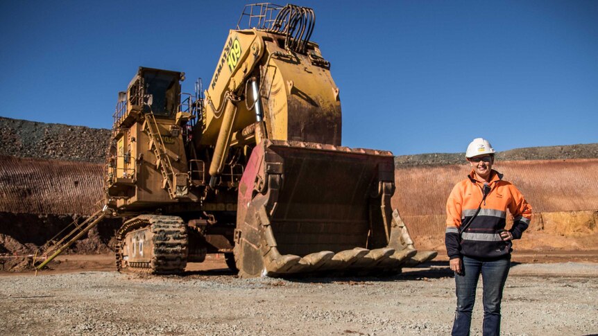 A female mine worker inside an open pit gold mine standing in front of machinery