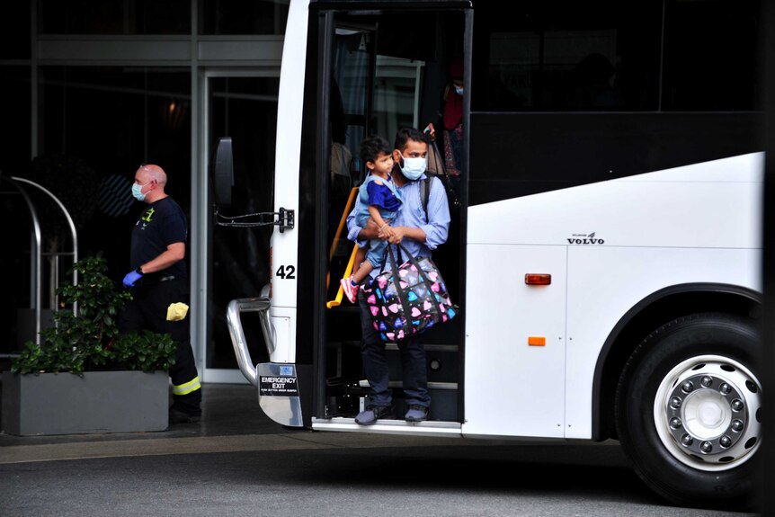 A man holds his child in his arms and walks off the front entrance of a white bus