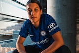 Sam Kerr, wearing a Chelsea kit, squats for a promo shot.