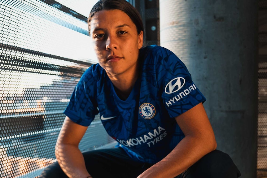 Sam Kerr, wearing a Chelsea kit, squats for a promo shot.