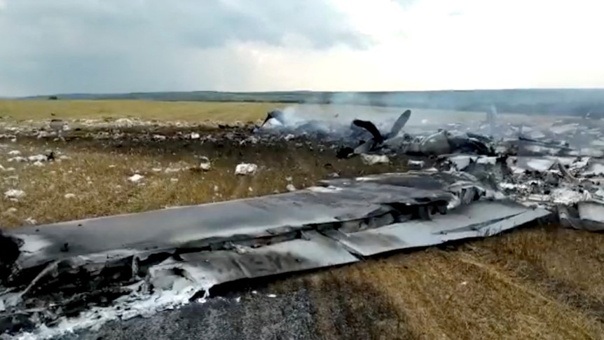 Smoke billows from the debris of what appears to be a plane wing, on the ground in a field