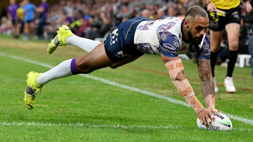 A Melbourne Storm NRL player plants the ball on the ground as he dives to score a try.