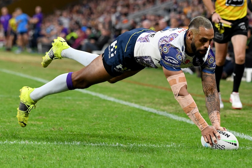A Melbourne Storm NRL player plants the ball on the ground as he dives to score a try.