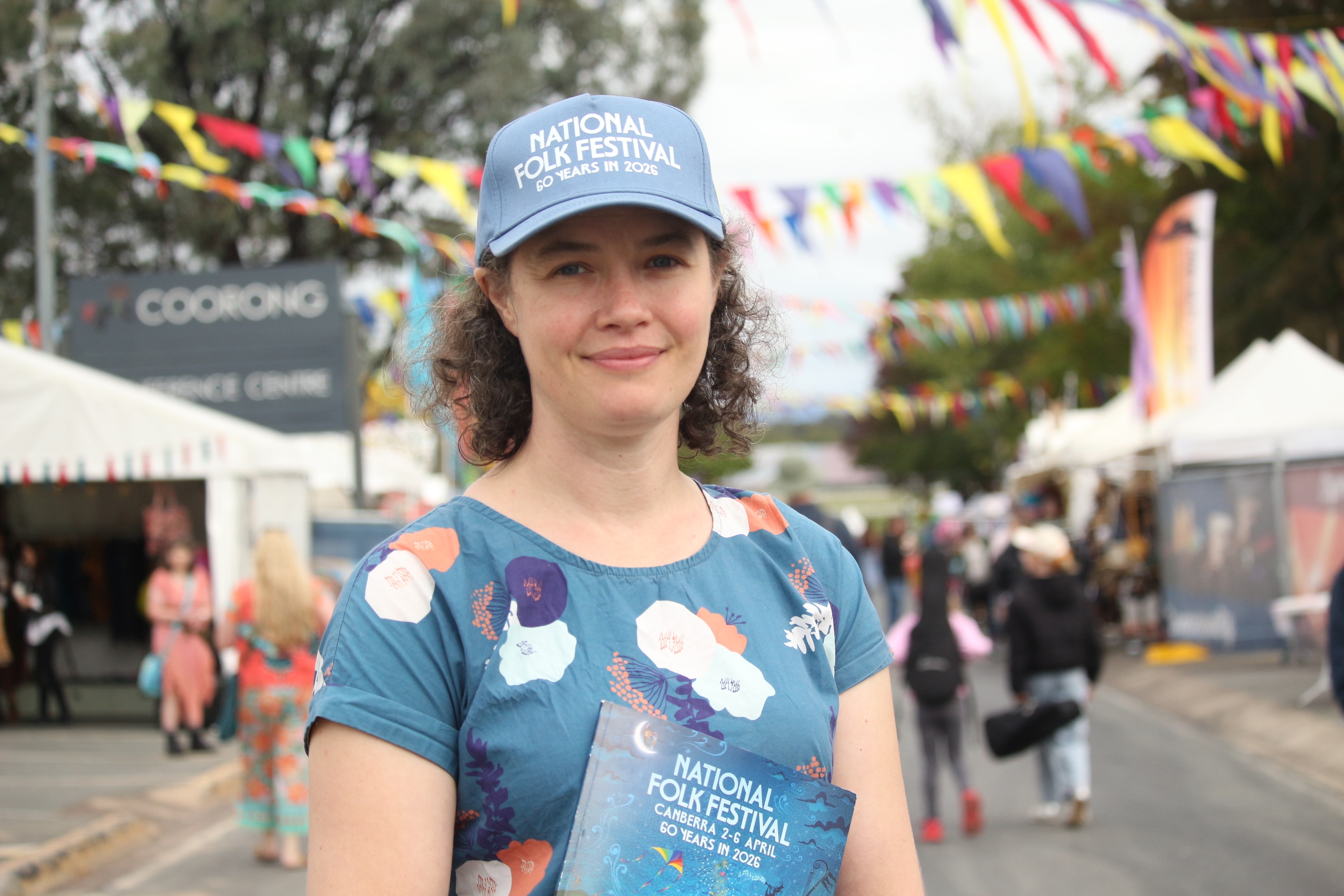 Una mujer lleva una gorra del Festival Folclórico Nacional y sostiene un folleto.