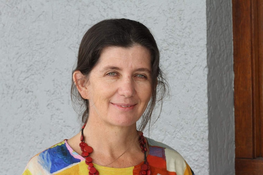 Close up of a woman smiling at the camera with a wall in the background.