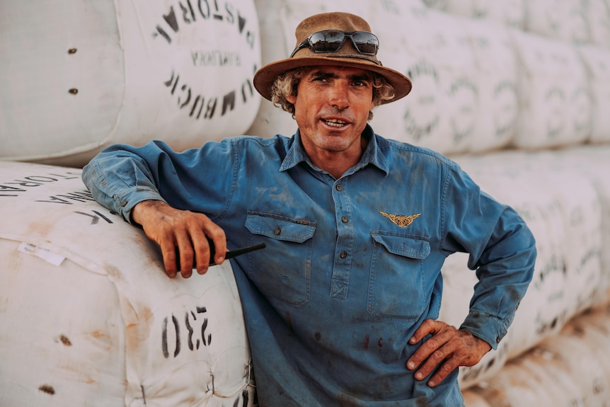 A man wearing a blue shirt and a hat, leaning against a stack of wool bales.