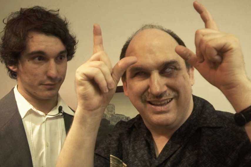 A man making a camera sign standing next to a man looking at him