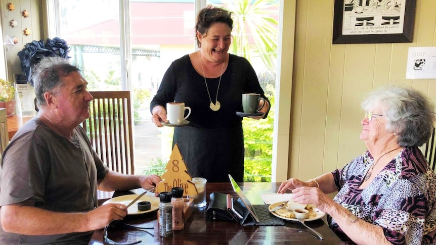 A barista serving two seated customers their coffee.