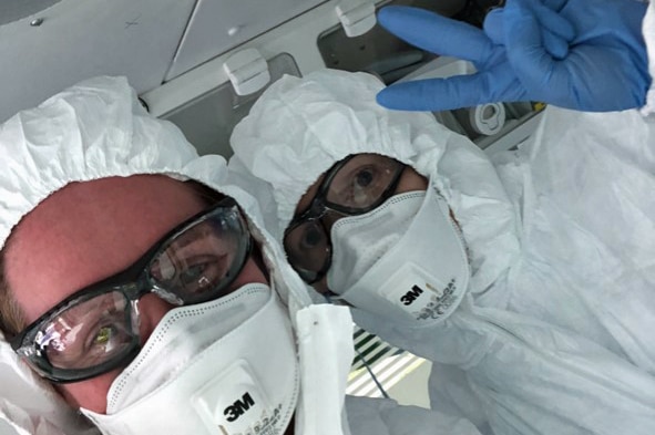 Two people wear personal protective equipment including masks, goggles, gloves and suits.