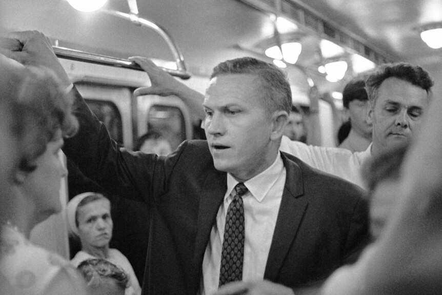 Black and white photo of a man in a suit on a subway 
