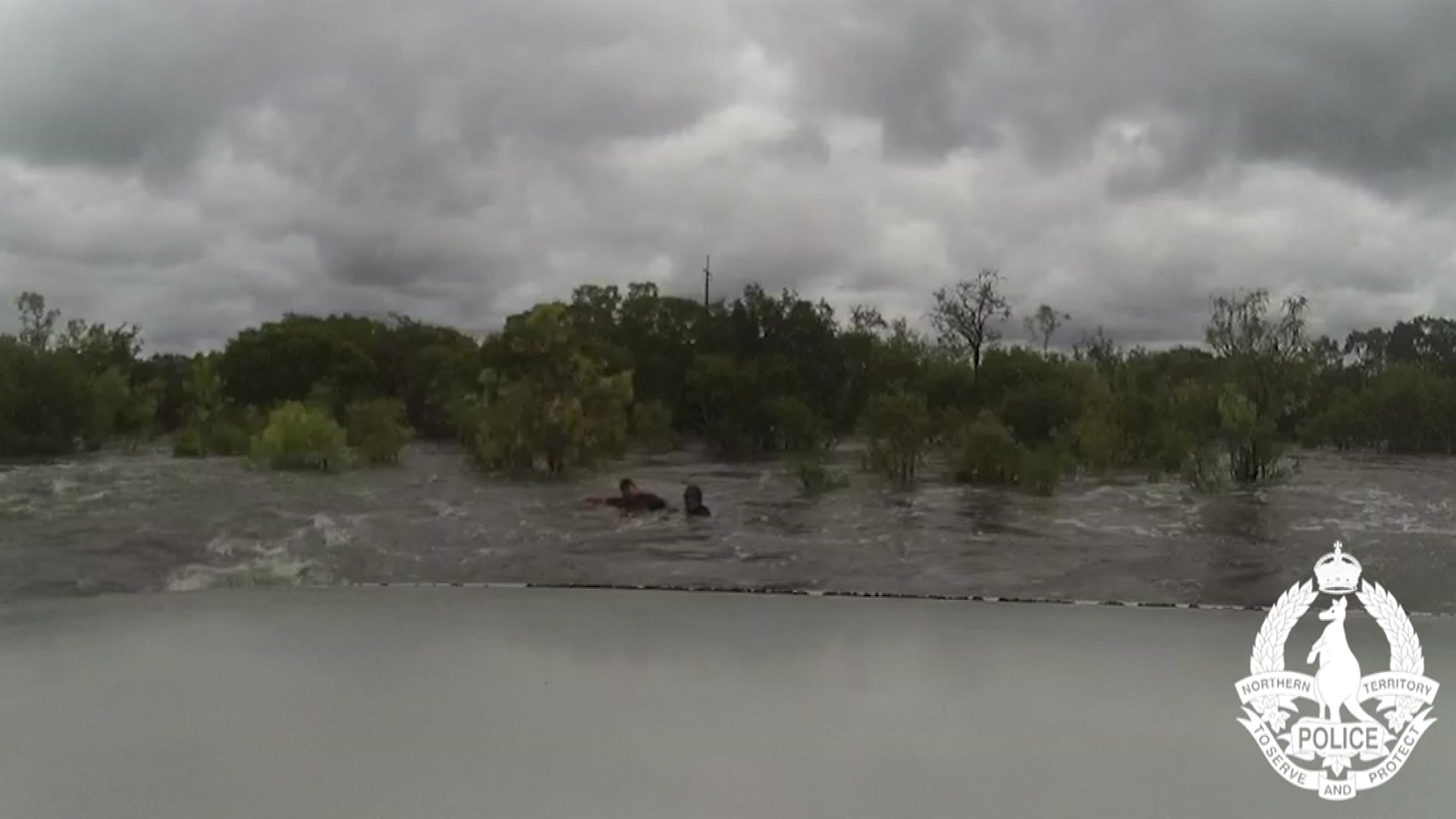 Two people wading through shoulder-height floodwaters.