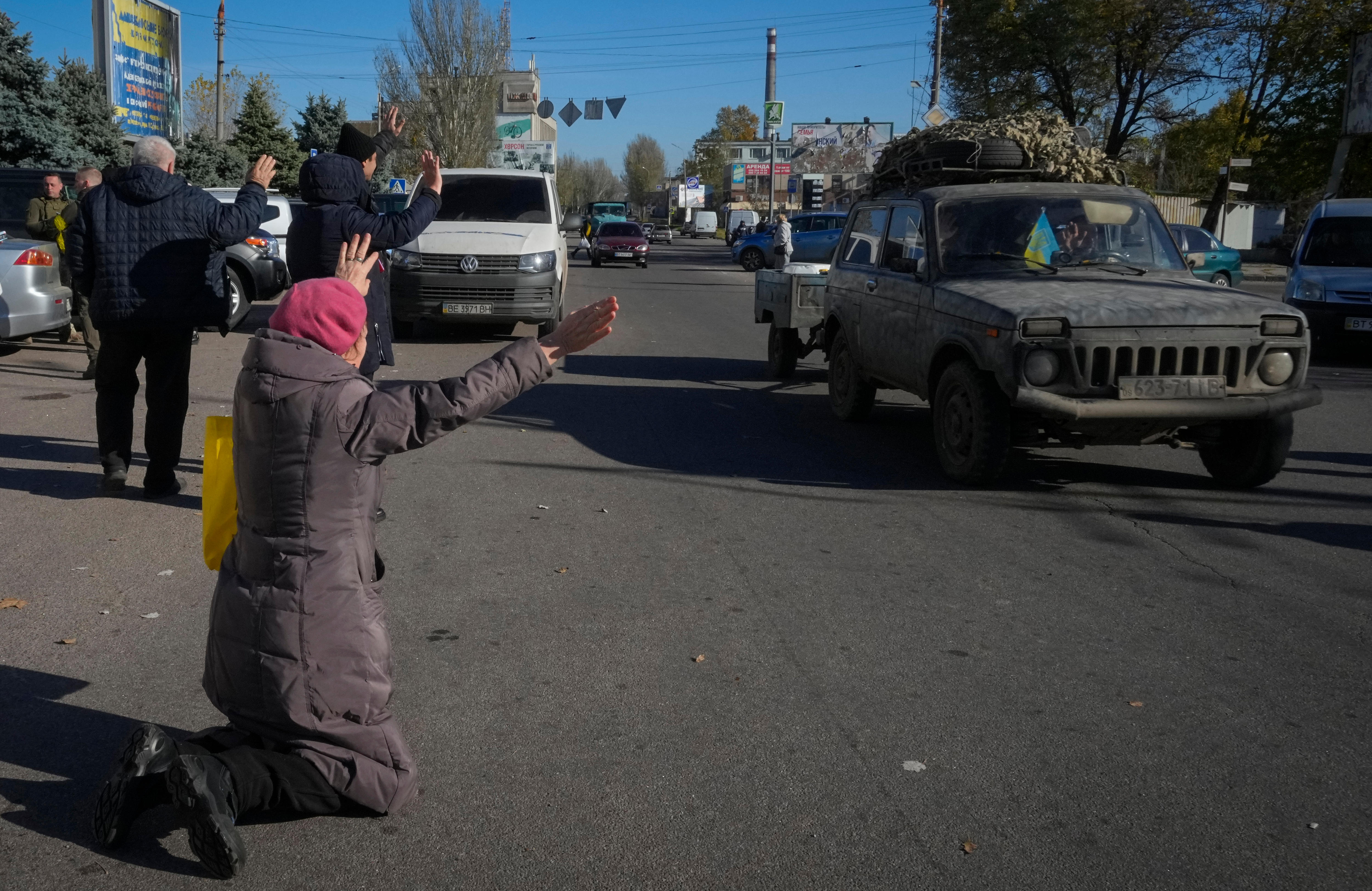 A woman kneels on the road as a car passes. 