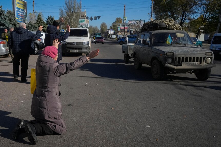 A woman kneels on the road as a car passes. 