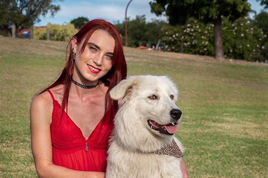 A woman in a red dress sitting on grass with a white dog.