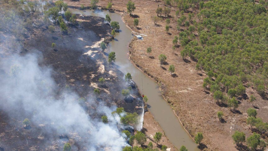 An aerial view of a helicopter dumping water on a fire near a river.