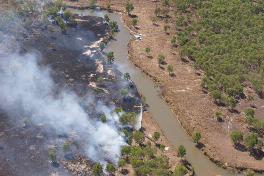 An aerial view of a helicopter dumping water on a fire near a river.