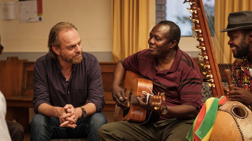 Actors Hugo Weaving and Andrew Luri in a scene from the film  Hearts and Bones, Andrew is playing a guitar in a choir