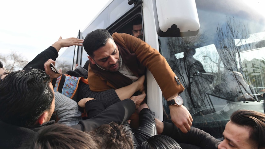 People struggle to get onto a bus as a crowd pushes towards the crowded doorway.